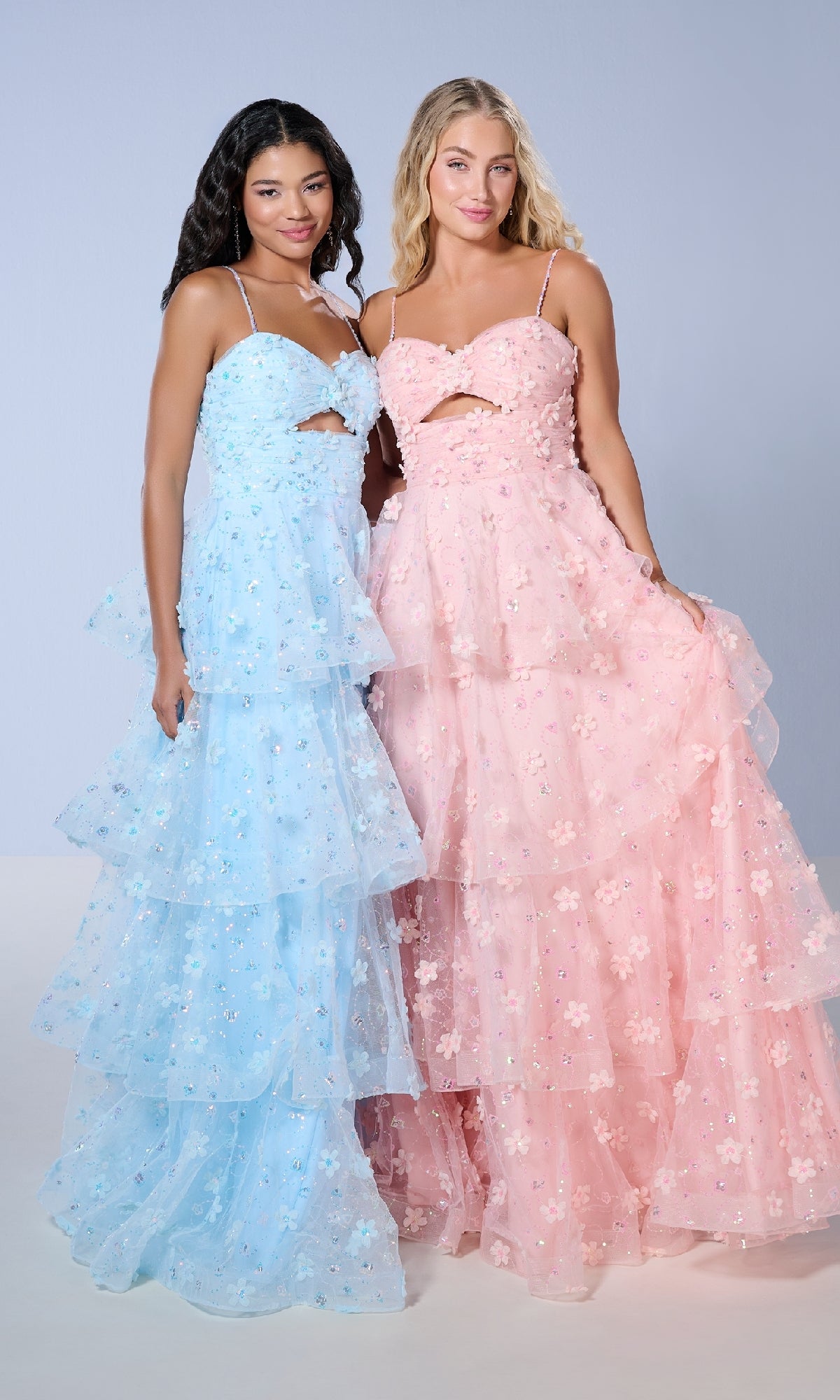 Two women stand side by side in Tiffany 16144 long prom dresses—one in light blue, the other in light pink. Both feature thin straps, cut-out details, 3D floral embellishments, and a tiered ruffled A-line skirt for a whimsical look.